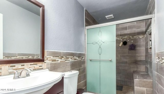 bathroom with walk in shower, vanity, a textured ceiling, tile walls, and toilet