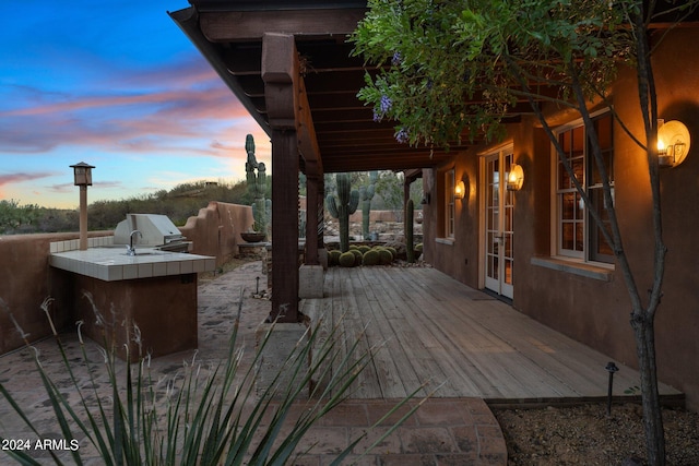 deck at dusk with french doors, exterior kitchen, and grilling area