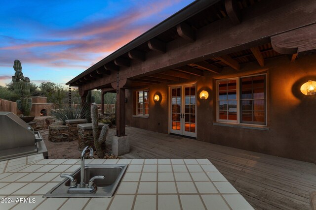 patio terrace at dusk with french doors, a grill, and a wooden deck