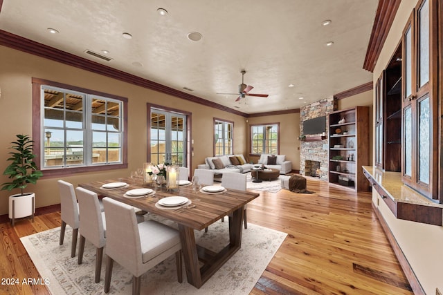 dining room with crown molding, light wood-type flooring, built in shelves, a stone fireplace, and ceiling fan