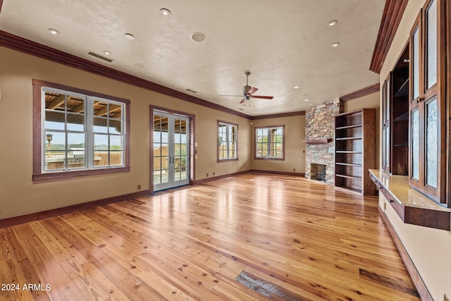 unfurnished living room featuring light hardwood / wood-style flooring, a fireplace, ceiling fan, ornamental molding, and built in shelves