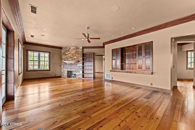 unfurnished living room with a stone fireplace, ornamental molding, light wood-type flooring, and ceiling fan