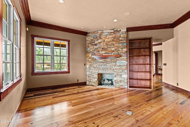 unfurnished living room with built in shelves, a stone fireplace, light hardwood / wood-style flooring, and crown molding