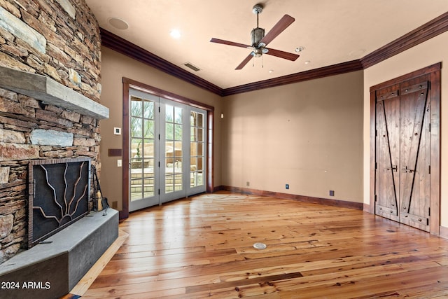 unfurnished living room featuring a stone fireplace, ornamental molding, light wood-type flooring, and ceiling fan