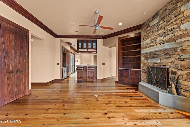 unfurnished living room featuring a stone fireplace, ceiling fan, crown molding, hardwood / wood-style floors, and built in shelves