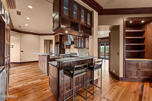 kitchen with kitchen peninsula, backsplash, a kitchen breakfast bar, stone counters, and hardwood / wood-style floors