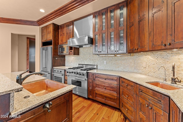 kitchen featuring light stone countertops, light wood-type flooring, appliances with stainless steel finishes, backsplash, and sink