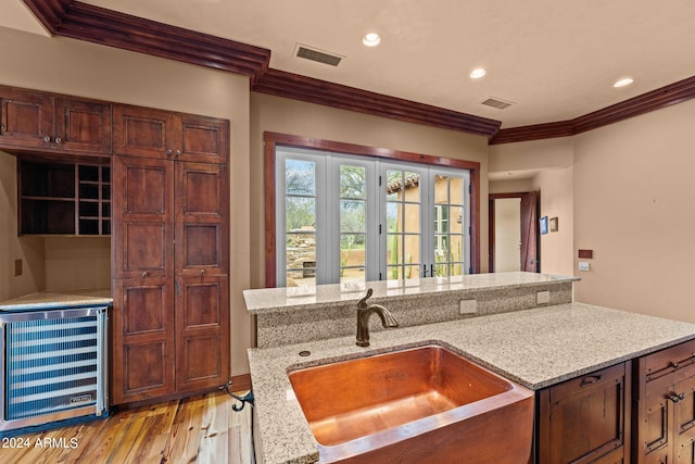 kitchen with crown molding, wine cooler, light stone countertops, light wood-type flooring, and sink