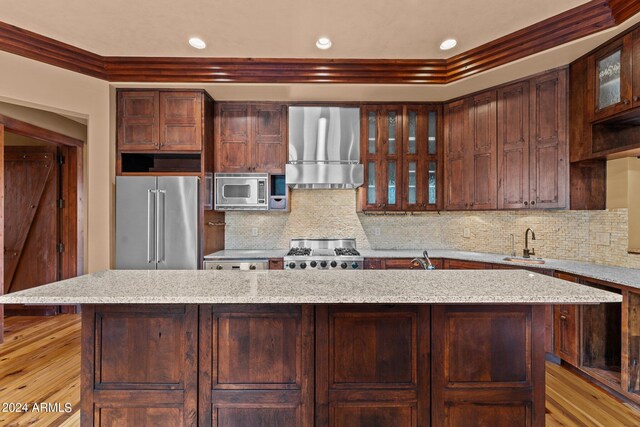 kitchen featuring a kitchen island, exhaust hood, tasteful backsplash, light wood-type flooring, and appliances with stainless steel finishes