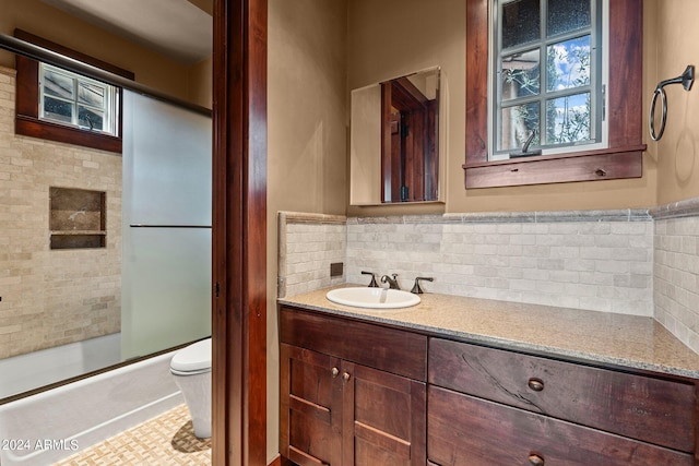 full bathroom with combined bath / shower with glass door, backsplash, tile floors, toilet, and large vanity