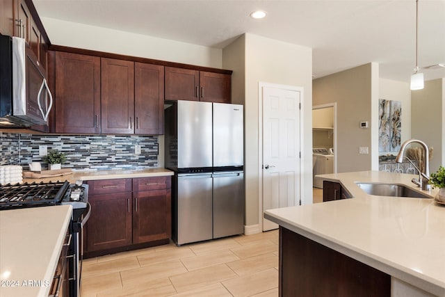 kitchen with a sink, stainless steel appliances, washer and clothes dryer, backsplash, and light countertops