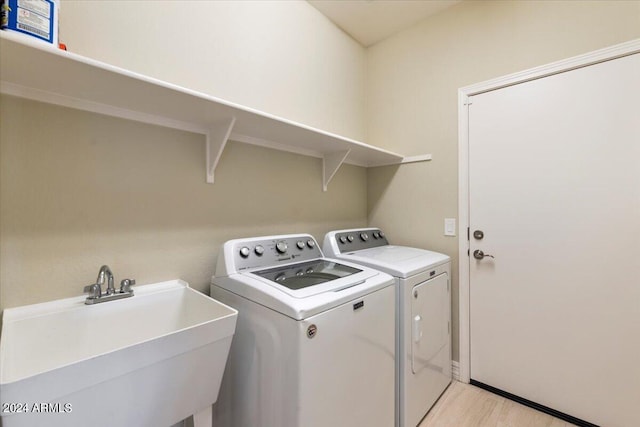 laundry room with light wood-type flooring, washer and dryer, and sink