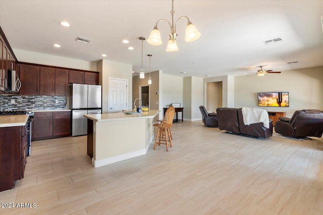 kitchen with tasteful backsplash, ceiling fan with notable chandelier, a center island with sink, stainless steel appliances, and hanging light fixtures