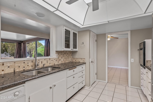 kitchen with decorative backsplash, white dishwasher, sink, dark stone countertops, and white cabinetry