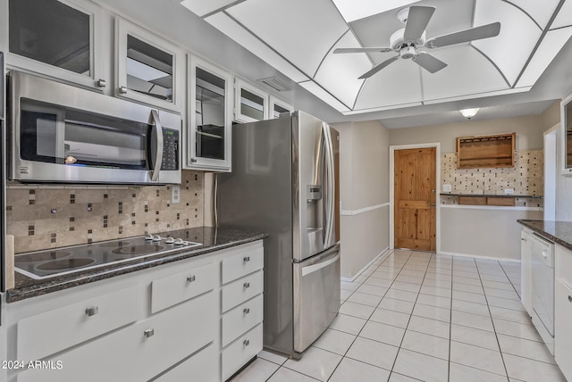 kitchen featuring appliances with stainless steel finishes, tasteful backsplash, light tile patterned floors, dark stone countertops, and white cabinets