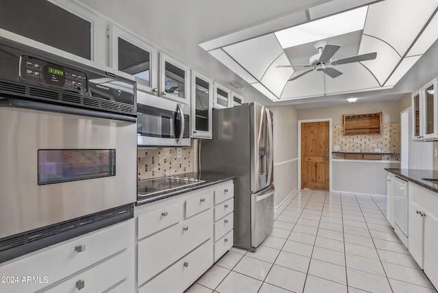 kitchen with tasteful backsplash, stainless steel appliances, light tile patterned floors, dark stone countertops, and white cabinetry