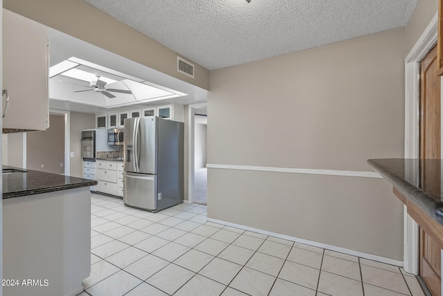 kitchen with a skylight, white cabinets, a textured ceiling, and appliances with stainless steel finishes