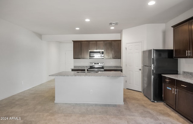 kitchen with dark brown cabinets, sink, an island with sink, stainless steel appliances, and light stone countertops