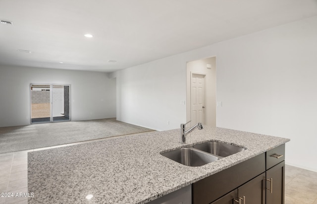 kitchen featuring light stone counters, light tile patterned floors, dark brown cabinetry, and sink