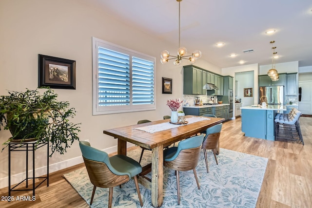 dining space with baseboards, light wood-style flooring, visible vents, and a notable chandelier