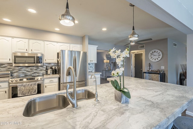 kitchen with tasteful backsplash, decorative light fixtures, stainless steel appliances, light stone countertops, and white cabinets