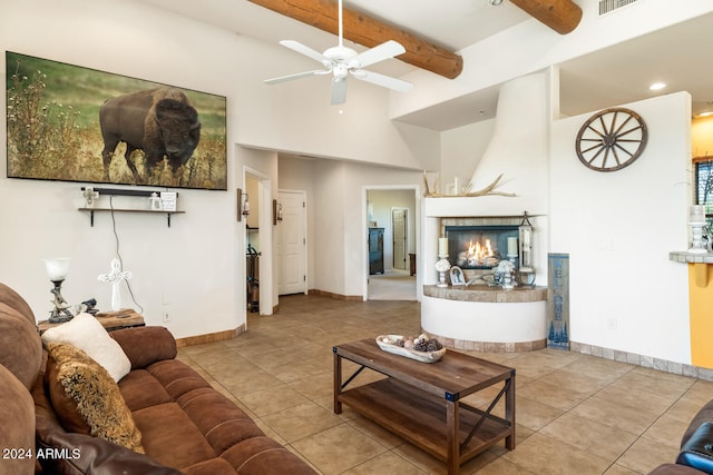 tiled living room with a fireplace, a high ceiling, beam ceiling, and ceiling fan