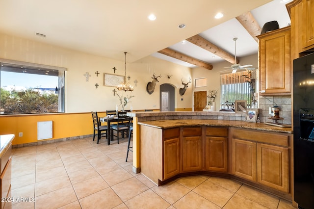 kitchen featuring beamed ceiling, a breakfast bar, black fridge, pendant lighting, and ceiling fan with notable chandelier