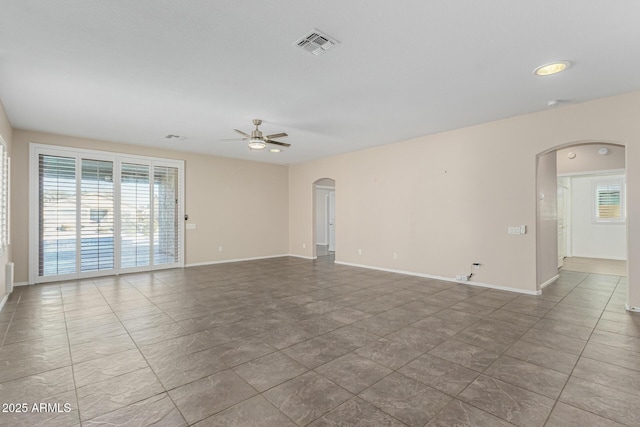 tiled empty room featuring visible vents, arched walkways, ceiling fan, and baseboards