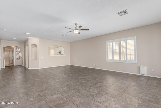 unfurnished living room with ceiling fan, visible vents, arched walkways, and baseboards