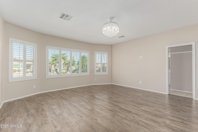 spare room with an inviting chandelier, light wood-style flooring, and visible vents