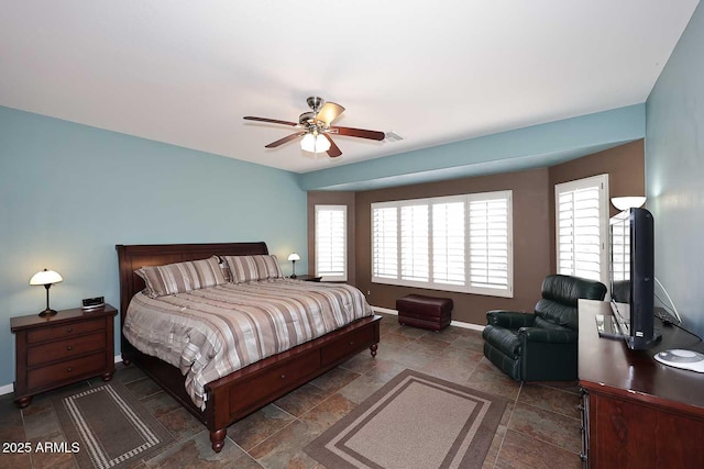 bedroom featuring stone finish floor, multiple windows, a ceiling fan, and baseboards