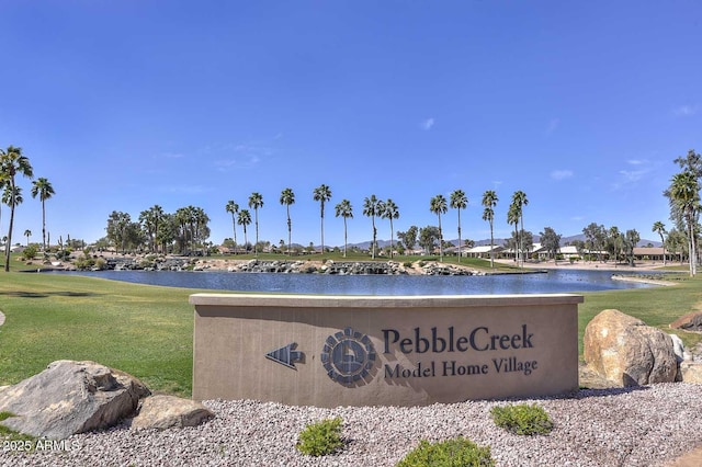 community sign featuring a lawn and a water view