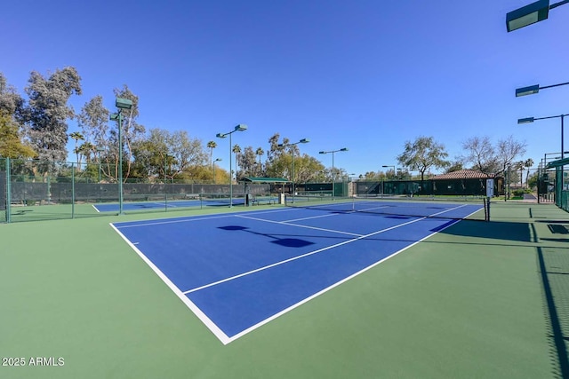 view of tennis court featuring community basketball court and fence