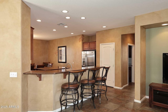 kitchen with baseboards, recessed lighting, stainless steel refrigerator with ice dispenser, a kitchen breakfast bar, and brown cabinets