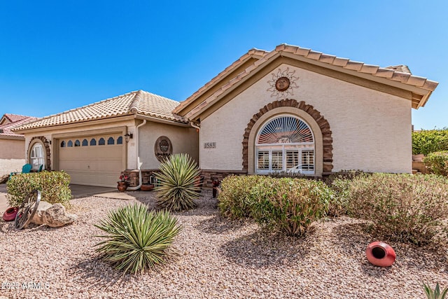 mediterranean / spanish house with stucco siding, stone siding, a garage, and a tiled roof