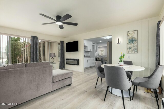 dining area with visible vents, a glass covered fireplace, a ceiling fan, and light wood-style floors