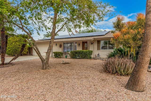 single story home featuring concrete driveway, brick siding, roof mounted solar panels, and an attached garage