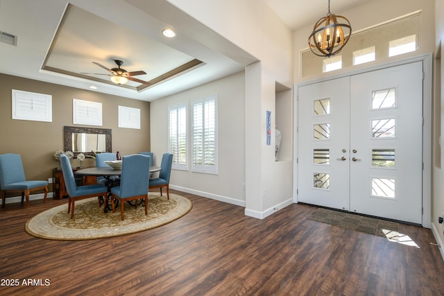 foyer entrance with a tray ceiling, dark wood-type flooring, french doors, and ceiling fan with notable chandelier