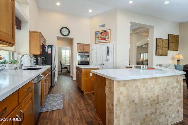 kitchen with sink, appliances with stainless steel finishes, a high ceiling, a kitchen island, and dark hardwood / wood-style flooring