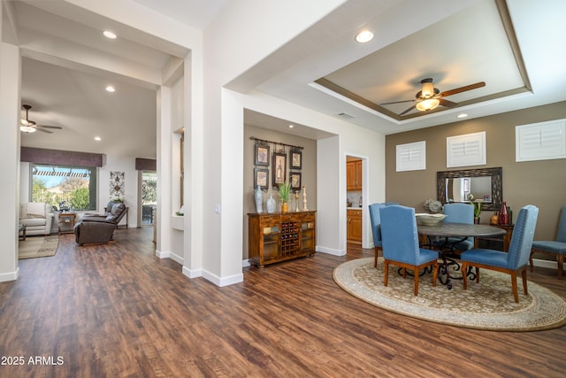 dining room with dark wood-type flooring, a raised ceiling, and ceiling fan