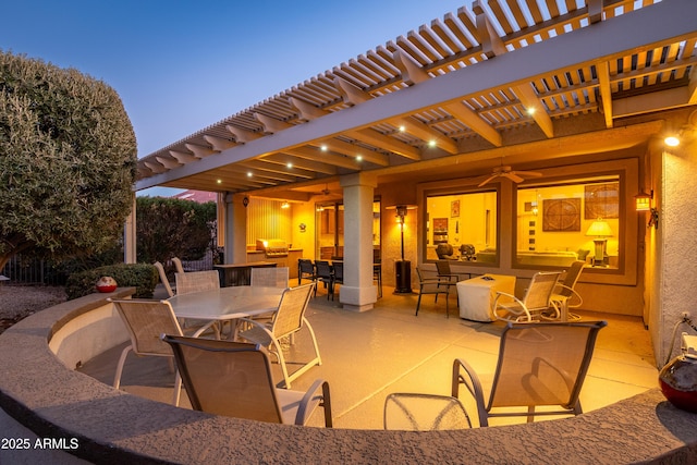 patio terrace at dusk featuring ceiling fan and a pergola