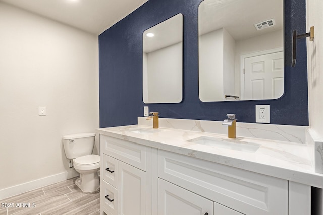 bathroom featuring wood finish floors, double vanity, visible vents, toilet, and a sink