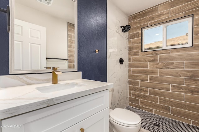 full bath with toilet, visible vents, tiled shower, and vanity