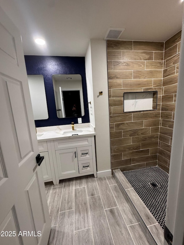 full bathroom featuring wood tiled floor, visible vents, tiled shower, and vanity