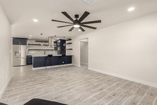 kitchen featuring a breakfast bar area, island range hood, light countertops, stainless steel refrigerator with ice dispenser, and open shelves