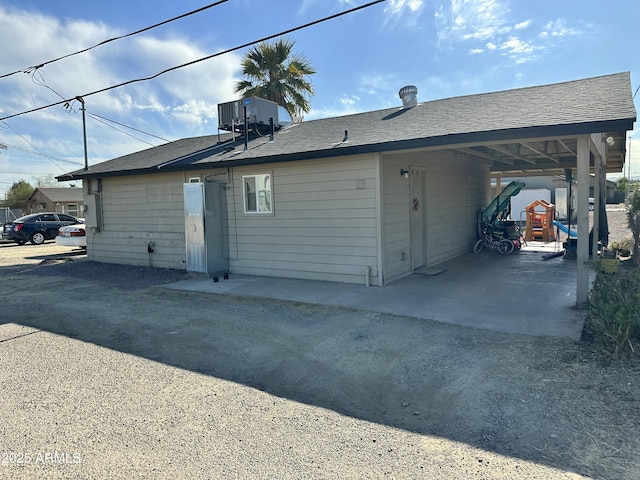 exterior space with driveway, a shingled roof, an attached carport, and central AC