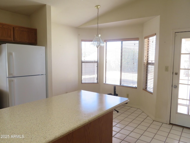 kitchen with freestanding refrigerator, pendant lighting, brown cabinets, light tile patterned floors, and vaulted ceiling