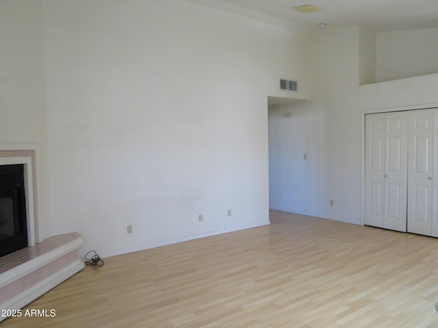 unfurnished living room featuring a glass covered fireplace, high vaulted ceiling, wood finished floors, and visible vents