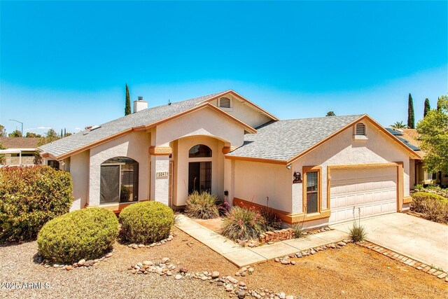 ranch-style home featuring an attached garage, a shingled roof, stucco siding, a chimney, and concrete driveway