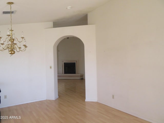 empty room featuring arched walkways, visible vents, a chandelier, and light wood-style floors